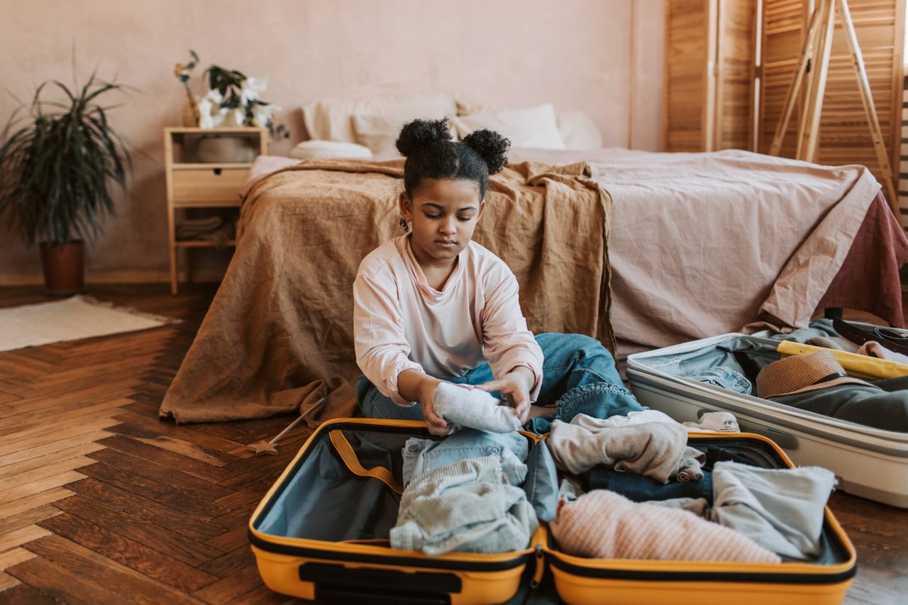 Child packing clothes into a suitcase before a family holiday