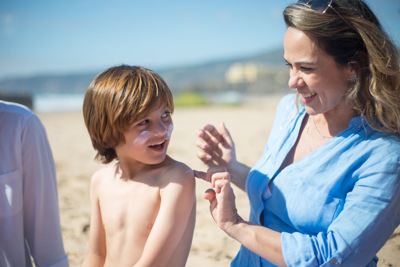 Mother applying sunscreen to her son on the beach
