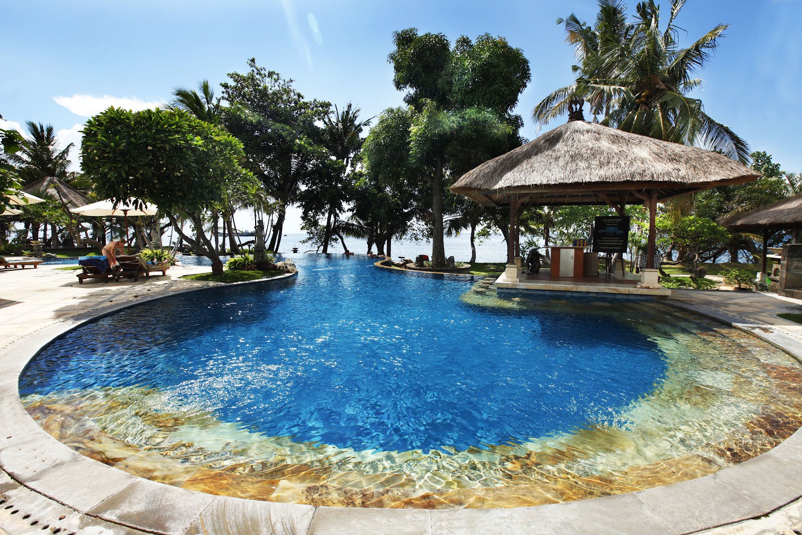 Lagoon swimming pool with thatched umbrellas near the beach in Lovina